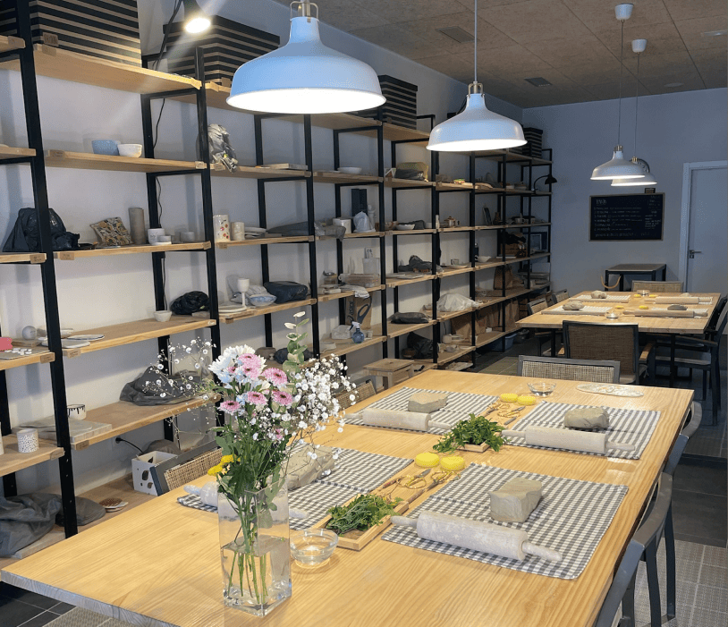 Aula de la escuela de cerámica Barroumami: mesa preparada con arcilla y rodillos, y estanterías con piezas al fondo